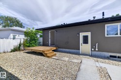 Gravel yard with a raised wood deck, chain link fencing, a concrete pathway, and a rear entry door - 