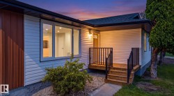White siding exterior with a dark shingle roof and a front porch featuring wood steps and black railings - 