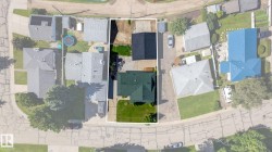 Property featuring a main residence with a green shingle roof, a detached structure with a dark shingle roof, a paved driveway, and a grassed yard - 