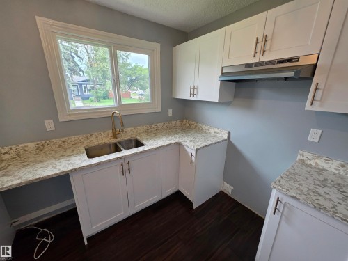 Kitchen featuring white shaker-style cabinetry, light-toned countertops, a stainless steel double basin sink with a brass-finish faucet, and coordinating hardware - 1907 145A Avenue Nw, Edmonton, AB - Indoor Photo Showing Kitchen With Double Sink