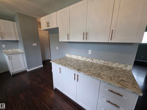 White shaker-style cabinetry with bronze-finish hardware, light-toned stone-finish countertops, and dark wood-finish flooring - 1907 145A Avenue Nw, Edmonton, AB - Indoor Photo Showing Kitchen