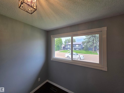Bright corner bedroom featuring expansive picture window with natural light, neutral paint finish, and textured ceiling detail - 1907 145A Avenue Nw, Edmonton, AB - Indoor Photo Showing Other Room