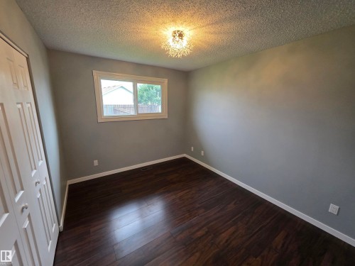 Wood-finish flooring, neutral wall tones, white bi-fold closet doors, and a decorative ceiling light fixture - 1907 145A Avenue Nw, Edmonton, AB - Indoor Photo Showing Other Room