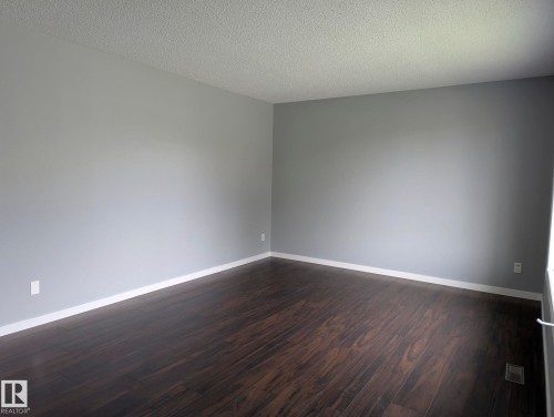 Spacious room featuring wood-finish flooring, light gray wall paint, white trim, and a textured ceiling - 1907 145A Avenue Nw, Edmonton, AB - Indoor Photo Showing Other Room