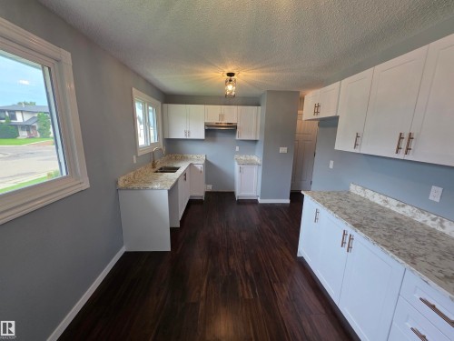 White cabinetry with brushed bronze hardware, wood-finish flooring, light-toned countertops, stainless steel sink with a gooseneck faucet, and recessed lighting - 1907 145A Avenue Nw, Edmonton, AB - Indoor Photo Showing Kitchen With Double Sink