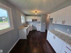 White cabinetry with brushed bronze hardware, wood-finish flooring, light-toned countertops, stainless steel sink with a gooseneck faucet, and recessed lighting - 