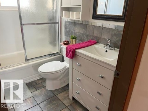 Bathroom featuring a white vanity with integrated sink, coordinating toilet, and a bathtub with frosted glass sliding doors - 5213 50 Avenue, Vegreville, AB - Indoor Photo Showing Bathroom