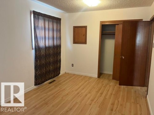 Room featuring wood-finish flooring, white baseboards, a built-in closet with double doors, and a ceiling-mounted light fixture - 5213 50 Avenue, Vegreville, AB - Indoor Photo Showing Other Room