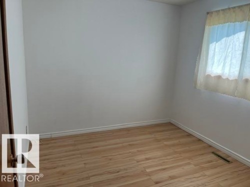 Room featuring wood-finish flooring, white baseboards, and a window with sheer curtains - 5213 50 Avenue, Vegreville, AB - Indoor Photo Showing Other Room