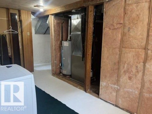 Utility area featuring exposed wood framing, ceiling-mounted lighting, visible insulation, and a water heater unit - 5213 50 Avenue, Vegreville, AB - Indoor Photo Showing Basement