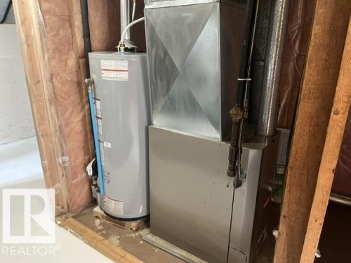 Water heater and furnace with exposed ductwork and utility piping, framed by unfinished wall studs and insulation - 5213 50 Avenue, Vegreville, AB - Indoor Photo Showing Basement