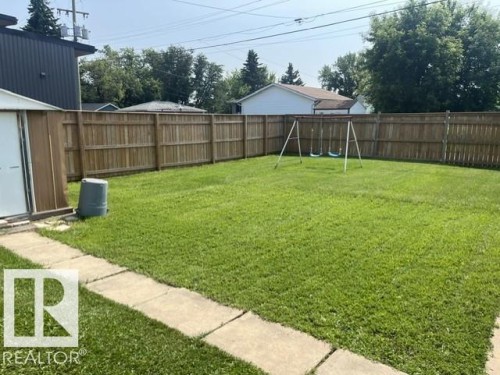 Expansive fenced yard featuring a manicured lawn, concrete paver pathway, and a storage shed - 5213 50 Avenue, Vegreville, AB - Outdoor With Backyard