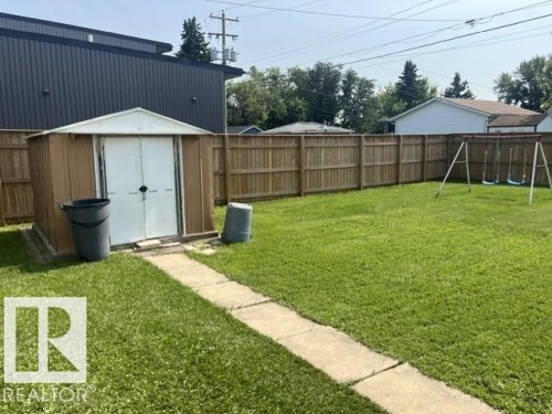 Expansive green lawn with a privacy fence, concrete path, and storage shed - 5213 50 Avenue, Vegreville, AB - Outdoor