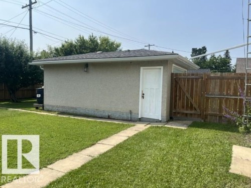 Detached stucco-exterior outbuilding featuring a white paneled door, gray shingle roof, and white rain gutters - 5213 50 Avenue, Vegreville, AB - Outdoor