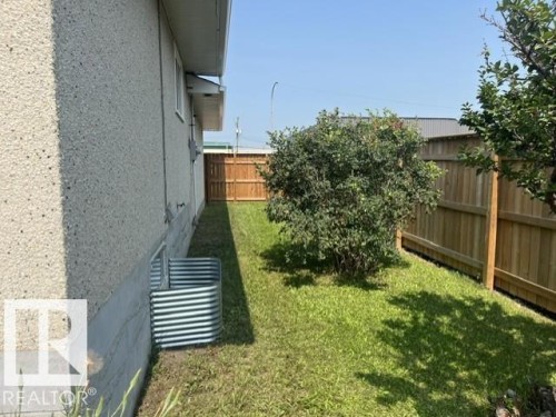 Exterior wall with stucco finish, a window well, and a fully fenced yard featuring a mature shrub and established grass - 5213 50 Avenue, Vegreville, AB - Outdoor