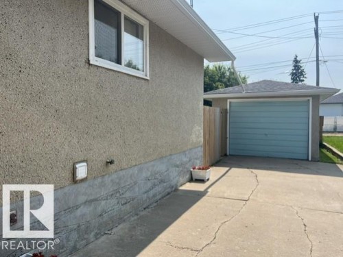 Detached garage with a light blue overhead door, concrete driveway, and side access - 5213 50 Avenue, Vegreville, AB - Outdoor With Exterior