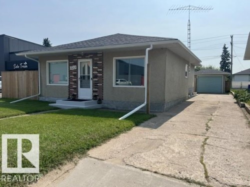 Single-story residence featuring a brick veneer accent wall, white storm door, and a well-maintained lawn - 5213 50 Avenue, Vegreville, AB - Outdoor