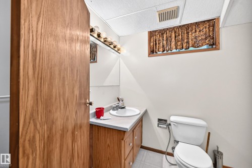 Compact half bath featuring a wood-finish vanity cabinet with an integrated sink, white ceramic toilet, and decorative window treatment - 6 Atkinson Place, St. Albert, AB - Indoor Photo Showing Bathroom