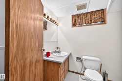 Compact half bath featuring a wood-finish vanity cabinet with an integrated sink, white ceramic toilet, and decorative window treatment - 