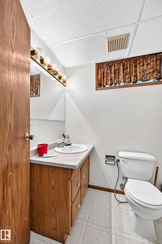 Compact bathroom featuring warm wood-finish cabinetry with integrated sink and countertop, white ceramic tile flooring, white subway tile walls, and standard white porcelain toilet with chrome fixtures - 6 Atkinson Place, St. Albert, AB - Indoor Photo Showing Bathroom