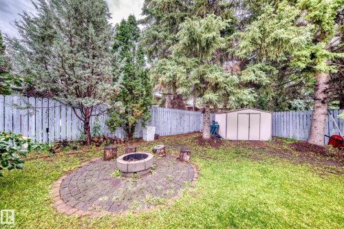 Private backyard oasis featuring a circular paver patio with integrated fire pit, mature landscaping with mixed evergreen and deciduous trees, lush lawn, and privacy fencing - 6 Atkinson Place, St. Albert, AB - Outdoor