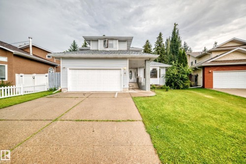 Welcoming two-story residence showcasing a white garage door, composite driveway with defined walkway, and manicured front lawn bordered by mature evergreen landscaping - 6 Atkinson Place, St. Albert, AB - Outdoor With Facade