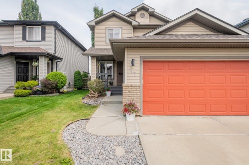 Two-story exterior with light beige siding, an attached garage featuring a bright orange door, a concrete driveway, and a front walkway with decorative gravel accents - 47 Landon Crescent, Spruce Grove, AB - Outdoor With Facade