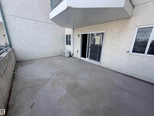 Private concrete patio with stucco exterior, a sliding glass door, and an exterior window - #208 6710 158 Av Nw, Edmonton, AB - Outdoor With Exterior