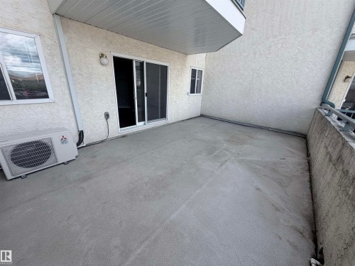 Spacious concrete patio with sliding glass door access, exterior wall sconce, and an air conditioning unit - #208 6710 158 Av Nw, Edmonton, AB - Outdoor With Exterior