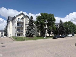 Multi-level building with individual balconies, gabled rooflines, and mature evergreen landscaping - 
