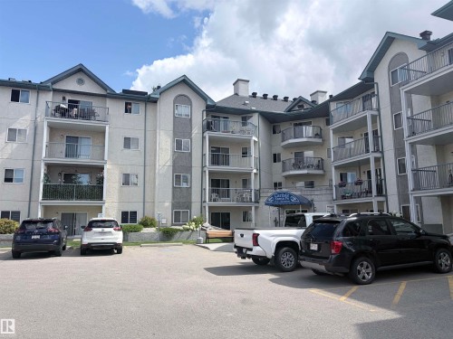 Multi-story building featuring balconies with metal railings, a paved parking area, and mature landscaping - #208 6710 158 Av Nw, Edmonton, AB - Outdoor With Balcony With Facade