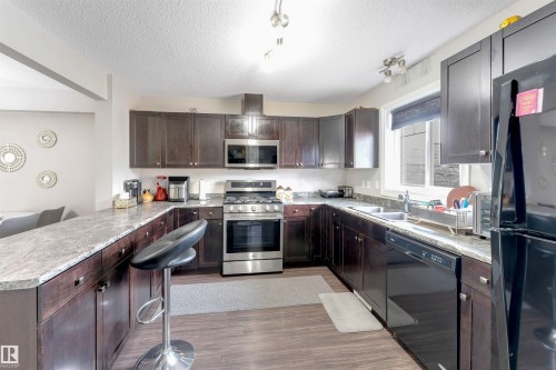U-shaped kitchen featuring dark wood cabinetry, light-toned countertops, wood-finish flooring, and stainless steel appliances - 3106 15 Avenue Nw, Edmonton, AB - Indoor Photo Showing Kitchen With Double Sink With Upgraded Kitchen