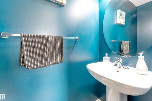 Pedestal sink with chrome faucet, circular mirror, and wall-mounted towel bars - 3106 15 Avenue Nw, Edmonton, AB - Indoor Photo Showing Bathroom