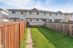 Fenced backyard with a grass lawn, concrete pathway, and a wood deck - 