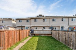 Rear exterior featuring a fenced yard with a grass lawn, paved pathway, and a wood deck with lattice railing - 