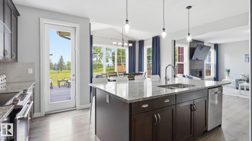Chef's kitchen featuring a large center island with prep sink, stainless steel appliances, quartz countertops, dark cabinetry with hardware accents, pendant lighting, and abundant natural light from multiple windows overlooking the grounds - 63 Rosemount Boulevard, Beaumont, AB - Indoor Photo Showing Kitchen With Double Sink With Upgraded Kitchen