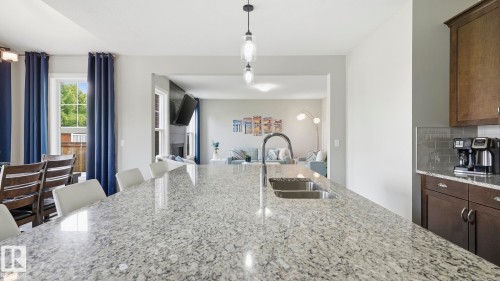 Expansive kitchen featuring a polished stone countertop with waterfall edge, stainless steel undermount sink with gooseneck faucet, dark cabinetry, and pendant lighting - 63 Rosemount Boulevard, Beaumont, AB - Indoor Photo Showing Kitchen With Double Sink