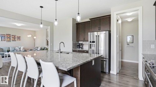 Kitchen island with granite countertop, stainless steel appliances, dark wood-finish cabinetry, and wood-finish flooring - 63 Rosemount Boulevard, Beaumont, AB - Indoor Photo Showing Kitchen With Upgraded Kitchen