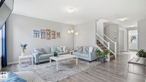 Bright, open-concept living area featuring plush seating arrangements, wood-finish flooring throughout, and abundant natural light from large windows - 63 Rosemount Boulevard, Beaumont, AB - Indoor Photo Showing Living Room