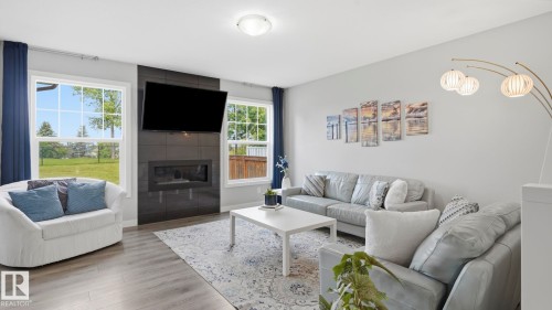 Spacious living area featuring wood-finish flooring, a contemporary fireplace with dark tile surround, and multiple windows - 63 Rosemount Boulevard, Beaumont, AB - Indoor Photo Showing Living Room With Fireplace