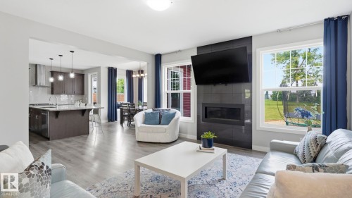 Open concept living space with wood-finish flooring, a contemporary fireplace, and multiple windows - 63 Rosemount Boulevard, Beaumont, AB - Indoor Photo Showing Living Room With Fireplace