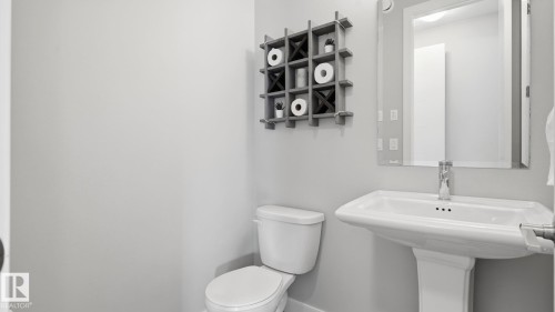 Clean and functional half bath featuring a pedestal sink with chrome faucet, white porcelain toilet, and neutral wall finishes - 63 Rosemount Boulevard, Beaumont, AB - Indoor Photo Showing Bathroom