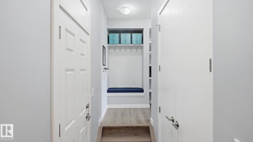 Bright hallway with multiple white six-panel doors, wood-finish flooring, recessed ceiling lighting, and built-in shelving with storage cubbies - 63 Rosemount Boulevard, Beaumont, AB - Indoor Photo Showing Other Room