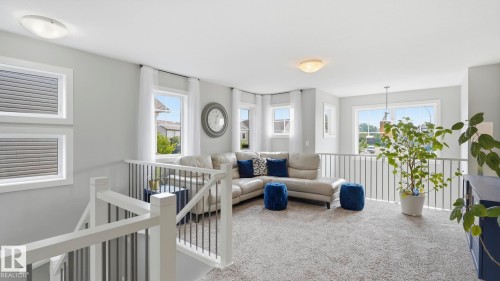 Bright, open-concept loft space featuring multiple windows with natural light, light gray carpeting, white railings and architectural detailing, recessed ceiling lighting, and abundant greenery from potted plants - 63 Rosemount Boulevard, Beaumont, AB - Indoor