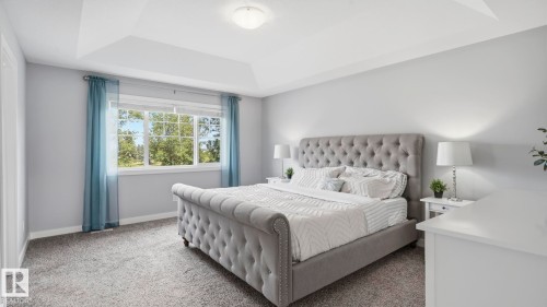 Master bedroom featuring a tufted upholstered bed frame, dual nightstands with table lamps, soft neutral wall finishes, carpeted flooring, and abundant natural light from multi-pane windows dressed in blue drapery - 63 Rosemount Boulevard, Beaumont, AB - Indoor Photo Showing Bedroom