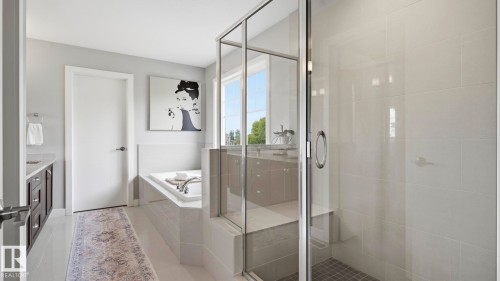 Spa-inspired primary bathroom showcasing a frameless glass-enclosed walk-in shower with tile surround, a freestanding soaking tub positioned near expansive windows, neutral tile flooring, and soft gray wall finishes that create a serene retreat - 63 Rosemount Boulevard, Beaumont, AB - Indoor Photo Showing Bathroom