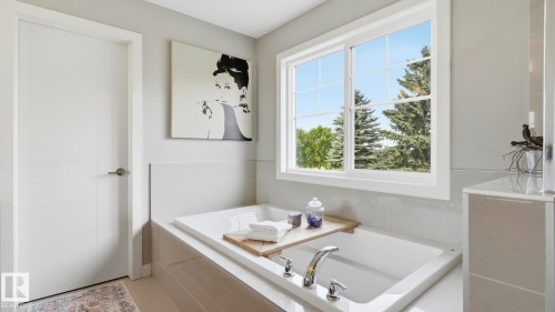 Built-in soaking tub with chrome fixtures, large window with grid pattern, light gray wall tile, and recessed cabinetry - 63 Rosemount Boulevard, Beaumont, AB - Indoor Photo Showing Bathroom