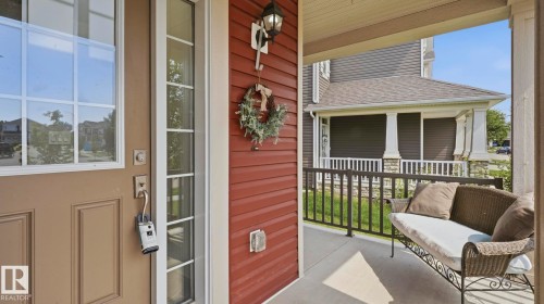 Covered front porch featuring black metal railings, wood-finish siding exterior in warm tones, large multi-pane windows with transom detailing, and a decorative wrought-iron bench - 63 Rosemount Boulevard, Beaumont, AB - Outdoor With Deck Patio Veranda With Exterior