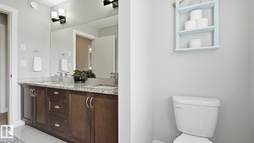 Dual vanity with dark wood-finish cabinetry, integrated sinks, and a large wall-mounted mirror - 63 Rosemount Boulevard, Beaumont, AB - Indoor Photo Showing Bathroom