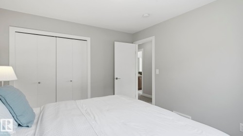 Serene primary bedroom showcasing soft neutral walls, abundant natural light, dual white panel closets with integrated hardware, and a spacious layout complemented by quality white bedding and coordinating blue accent pillows - 63 Rosemount Boulevard, Beaumont, AB - Indoor Photo Showing Bedroom